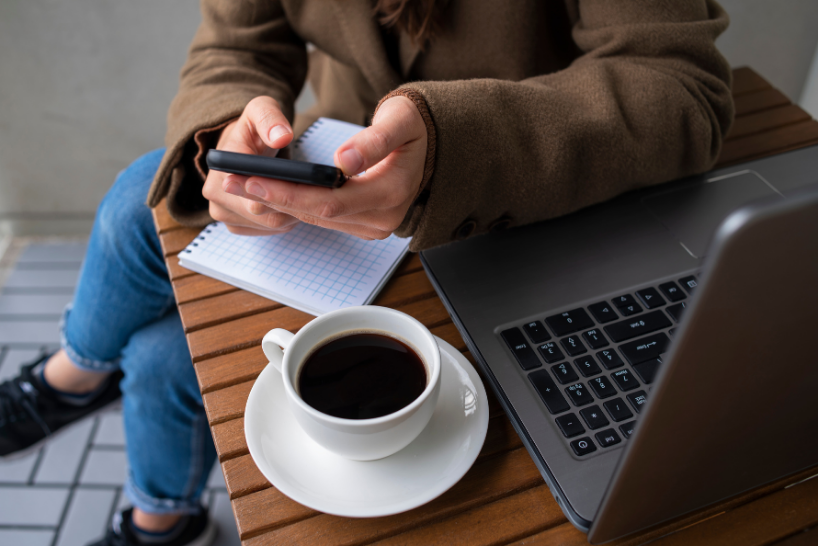 Person working on a laptop holding a mobile phone