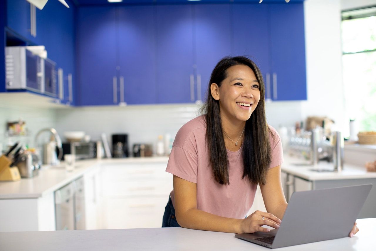 A woman working at a laptop from her brightly coloured kitchen A woman working at a laptop from her brightly coloured kitchen