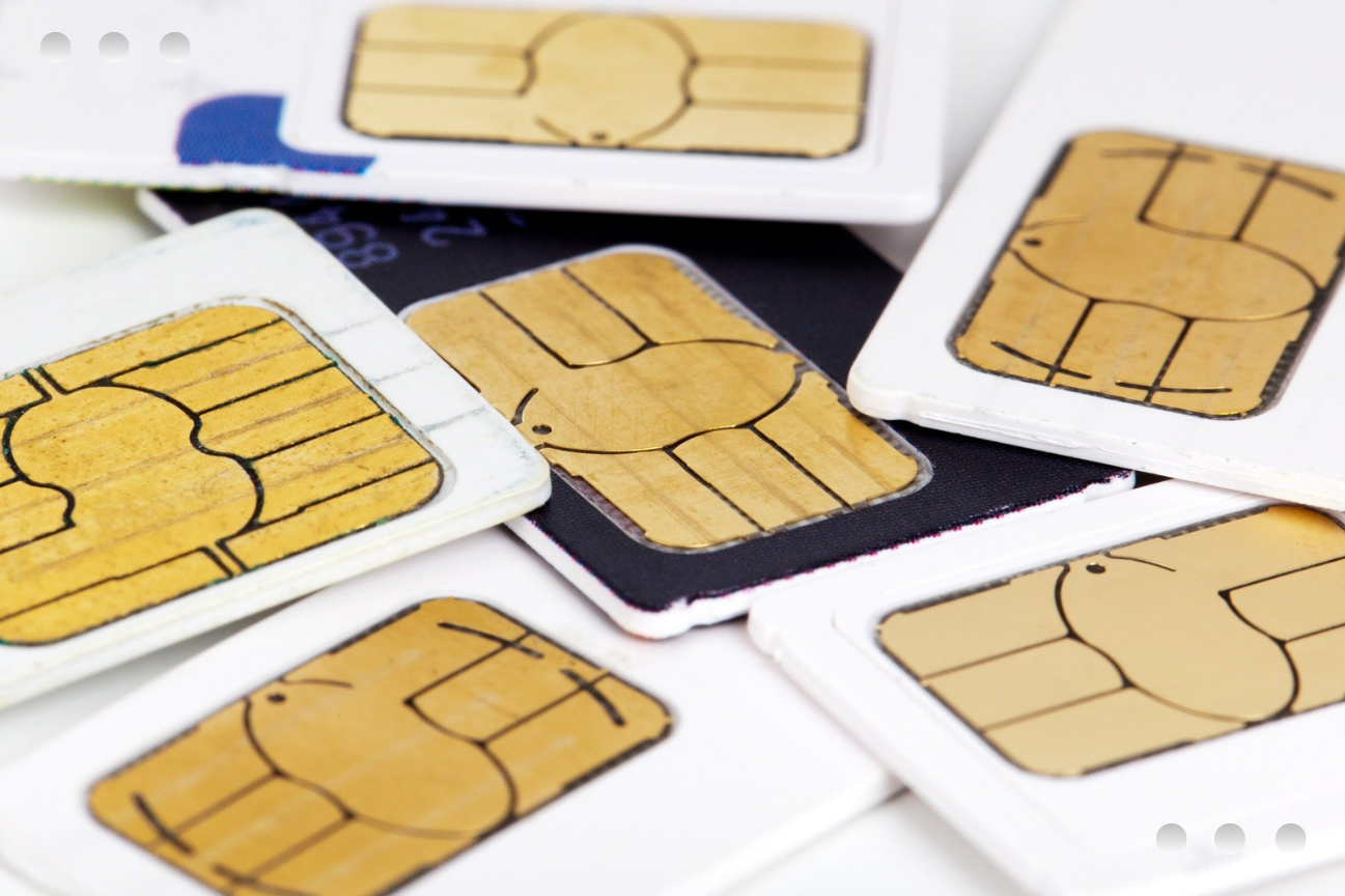A close-up, top-down view of several mobile phone SIM cards scattered and overlapping. Each card features a prominent rectangular gold contact chip, with most cards framed in white plastic and one in a black frame