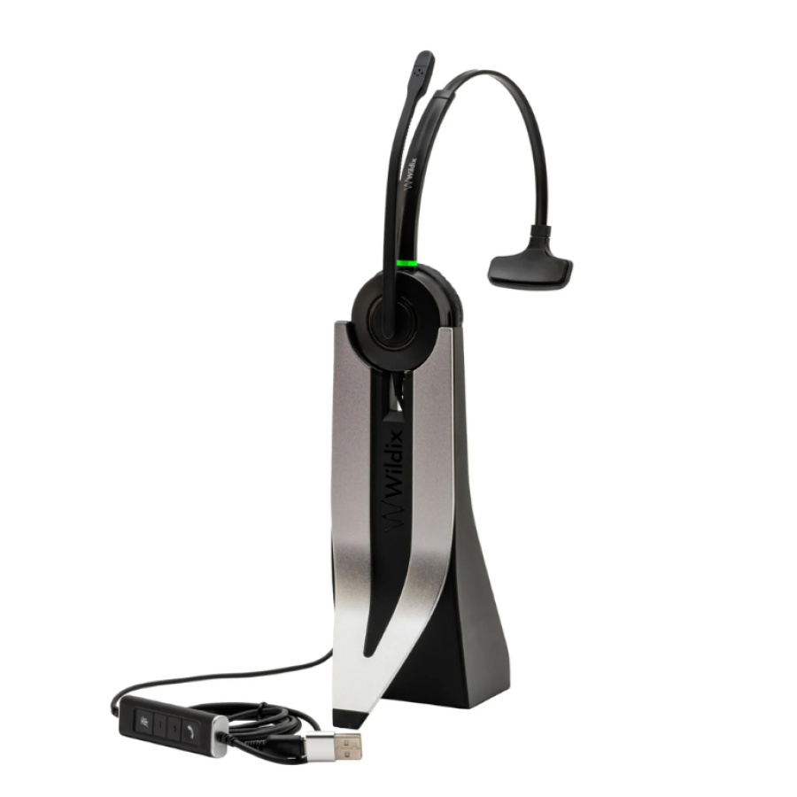 Wildix MonoLED single-ear wireless headset with boom microphone, resting on its charging stand with USB cable and inline call controls.