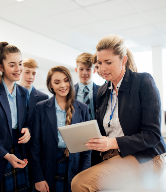 A teacher surrounded by pupils looking at a tablet device