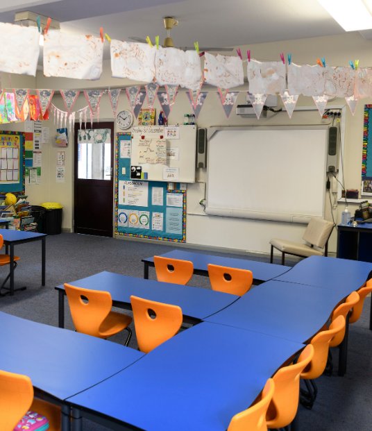 A classroom with blue tables and orange chairs, and a whiteboard